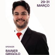 Foto de perfil do diretor do Procon RS, Rainer Grigolo, um homem branco de óculos de grau que está vestido em traje formal. Ele veste um terno preto, uma camisa branca e uma gravata vermelha.