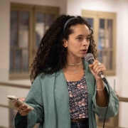 A diretora do Iecine, Sofia Ferreira, uma mulher negra de cabelos cacheados castanho, que veste uma tiara e uma camisa social azul marinho, fala ao microfone.

Autoria da descrição da foto: Wagner Meirelles Ascom SJCDH