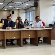 Em médio plano, estão quatro representantes da SJCDH sentados atrás da mesa no centro da sala. Da esquerda para a direita, estão a subsecretária de Direitos Humanos, Inclusão, Igualdade e Fraternidade, Marcia Scherer — uma mulher branca de óculos e cabelo loiro, liso e comprido que veste uma camisa branca; o secretário da SJCDH, Mateus Wesp, um homem branco de óculos e cabelo preto e curto, que veste um terno azul escuro, uma camisa social branca e uma gravata cor de vinho; a diretora do departamento da Igualdade Étnico-Racial, Sanny Figueiredo — uma mulher negra que usa uma camisa marrom escuro, um cachecol marrom claro e um turbante dourado com estampa em vermelho, branco e preto; e o diretor adjunto do departamento da Igualdade Étnico-Racial, Eduardo Feron, um homem negro com ascendência indígena de cabelo preto e curto, que veste uma camisa social branca.

Autoria da descrição da foto: Wagner Meirelles / Ascom SJCDH