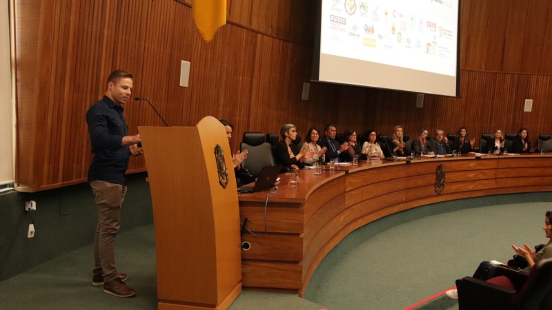 Em primeiro plano, o diretor João Pedro Albuquerque de Azevedo, um homem branco de cabelo loiro, que veste uma camisa social azul marinho e calça caqui bege, fala ao microfone no palanque do auditório do Ministério Público Gaúcho. À direita e ao fundo, as demais autoridades aparecem sentadas aplaudindo a sua fala.

Autoria da descrição da foto: Wagner Meirelles Ascom SJCDH