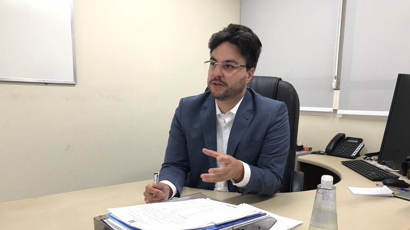 Em médio plano, está sentado em sua mesa de escritório o diretor do Procon RS, Rainer Grigolo, um homem brnaco de óculos e cabelo preto, que veste uma camisa social branca e um blazer azul marinho.
Autoria da descrição da foto: Wagner Meirelles Ascom SJCDH