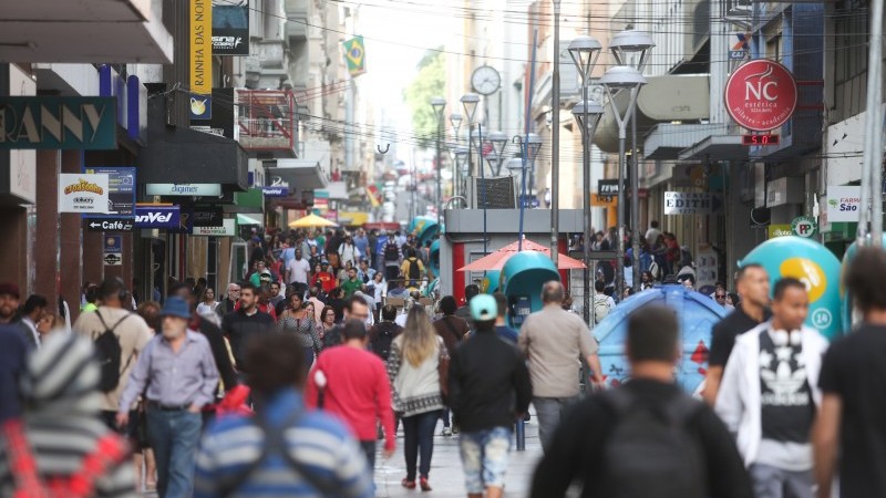 Na foto, há várias pessoas caminhando pela Rua dos Andradas, Centro Histórico de Porto Alegre, entre diversos estabelecimentos comerciais.