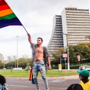  O homem balançando bandeira LGBT, utilizando sapato de salto alto, com CAFF de fundo