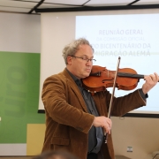 Violinista abre a reunião com uma apresentação. Atrás dele está o telão com banner da reunião geral. 
