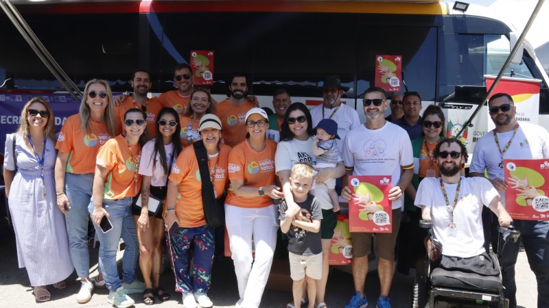 Cerca de 20 pessoas posam para foto embaixo de toldo armado na lateral do &ocirc;nibus do Procon, s&atilde;o membro das SJCDH e autoridades visitantes do espa&ccedil;o.