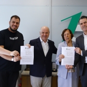 Cinco pessoas em p&eacute;, segurando o termo de colabora&ccedil;&atilde;o assinado, em frente a um balc&atilde;o, na sala da Secretaria de Justi&ccedil;a, Cidadania e Direitos Humanos.